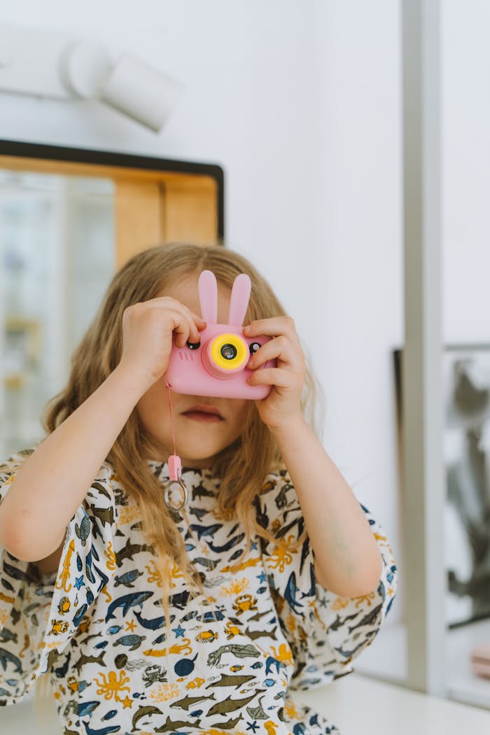 A child using a playful pink toy camera indoors, capturing joyful memories.